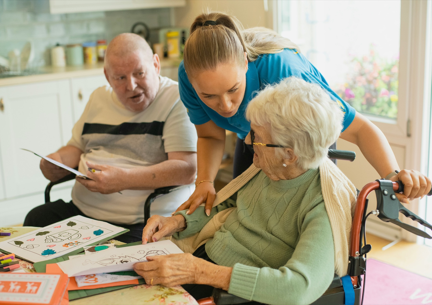 A care professional spending time with two older adults at a kitchen table